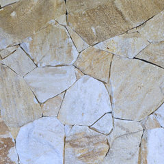 A close-up of a Cresta Beige Stone Cladding wall displays variously shaped, light brown and beige stones with visible gaps and seams, highlighting the freestyle walling technique.