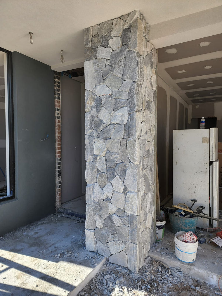 A Luna Grey Stone Cladding column stands at the entrance of a building under construction, surrounded by materials and debris. Inside, unfinished walls and exposed wires are visible. — Stone Cladding