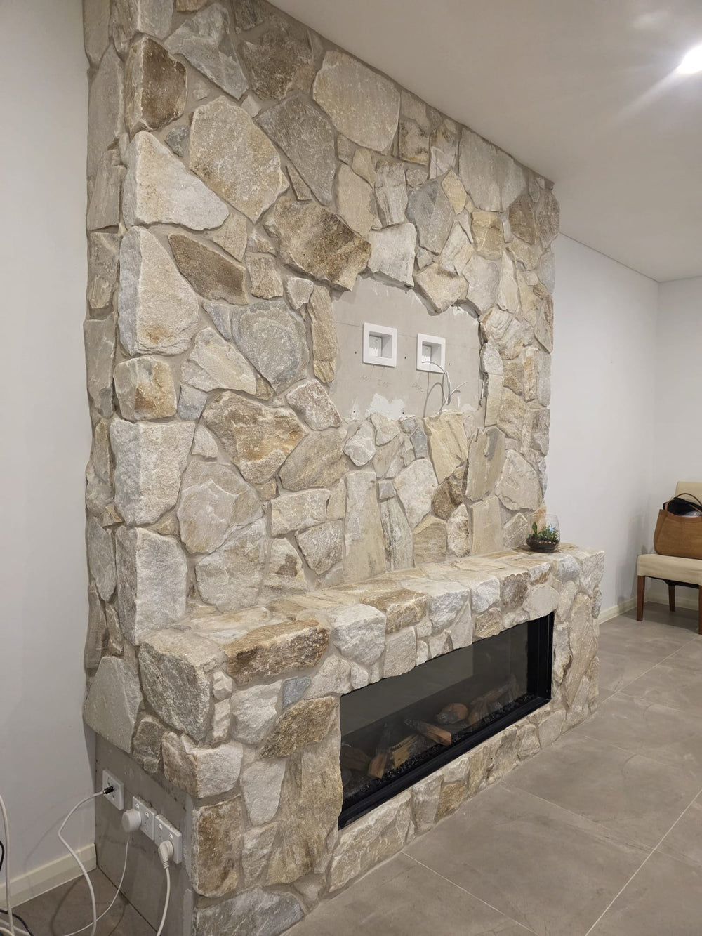 A close-up of a Cresta Beige Stone Cladding wall displays variously shaped, light brown and beige stones with visible gaps and seams, highlighting the freestyle walling technique.