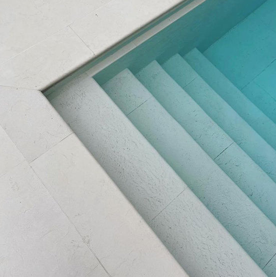 Galala Pearl Limestone Pavers in light gray create a minimalist, refined look for pool steps, with geometric lines and clear blue water enhancing the serene, clean atmosphere. — Natural Stone Paving